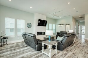 A spacious living room with a fireplace, leather sofas, a TV, and a ceiling fan. - Drift Away to the Beach - 5BR Beachside Home with Elevator & Easy Beach Access (Galveston)