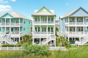 A beachfront property with multiple-story houses featuring balconies, a pool, and a white picket fence. - Drift Away to the Beach - 5BR Beachside Home with Elevator & Easy Beach Access (Galveston)