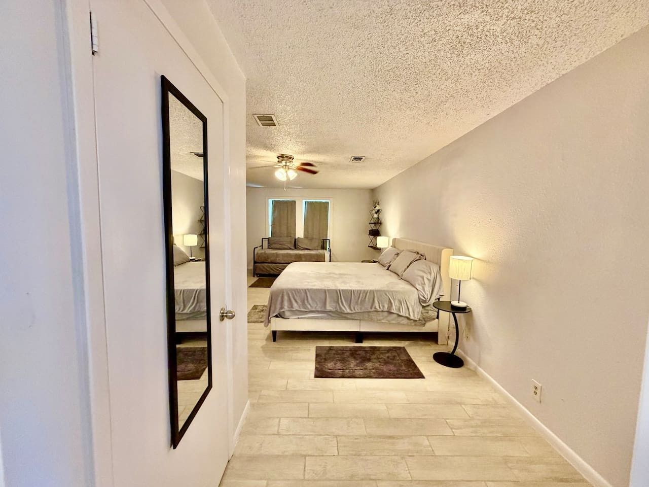 A bedroom with a bed, bedside tables, a ceiling fan, and a view of the adjacent room.