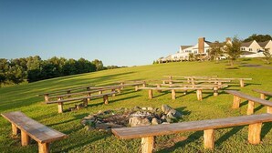 A grassy outdoor area with picnic tables and a fire pit, surrounded by trees and a building in the background. - Go to DC 250yr July 4th Celebration,  3 br Cabin at Shenandoah Crossing Resort (Gordonsville)