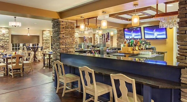 A bar area with wooden chairs, a counter with bottles, and stone walls.