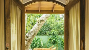 Una puerta de madera abierta que da a un patio con un banco de madera y un árbol.