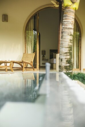 Uma área de piscina com uma espreguiçadeira, uma mesa de madeira e uma palmeira.