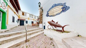 Una calle con escalones de piedra que conducen a un edificio con una escultura decorativa de pez y un cartel.