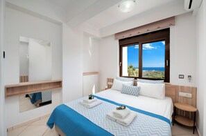 Ein Hotelzimmer mit einem großen Bett, einem Fenster mit Meerblick, einem Nachttisch und einem Spiegel.