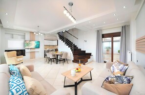 Ein modernes Wohnzimmer mit Sofa, Couchtisch und Fernseher. Eine Treppe führt zu einem Balkon.