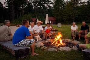 A group of people sitting around a campfire in a grassy outdoor area with trees in the background. - Cottage 32 | Pet-Friendly Forest View Muskoka Cottage Sleeps 6 (Muskoka Lakes)
