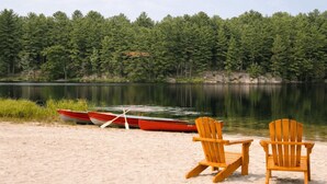 A beach with two wooden chairs and two red canoes tied to a dock.