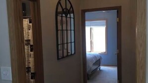 Ein Flur mit Holzrahmen einer Tür, einem Metallgitter und einem Bett im angrenzenden Zimmer.