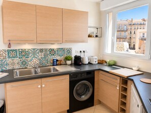 Eine moderne Küche mit Holzschränken, einer Waschmaschine und einem Fenster mit Blick auf die Stadt.