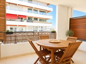 Ein Balkon mit rundem Holztisch und Stühlen, einer Korbuschlag und Topfpflanzen.