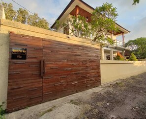 Una villa con un cancello in legno, un cartello con la scritta 'Singaraja Sea View Villa' e una casa moderna sullo sfondo.