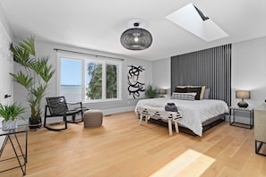 Une chambre moderne avec un grand lit, une vue sur la mer, un luminaire au plafond et une fenêtre.