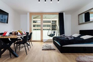 Een moderne kamer met een bed, een eettafel met stoelen, een televisie en een groot raam.