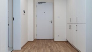 Un pasillo con una puerta blanca, suelo de madera y armarios blancos.