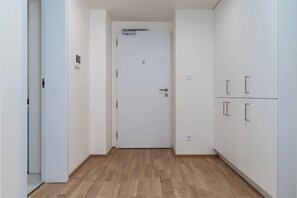 Een hal met een witte deur, houten vloer en witte kasten.