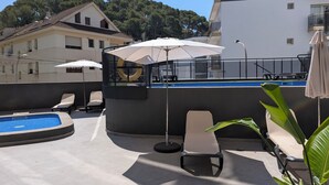 Un espace piscine aménagé sur le toit, avec des chaises longues, des parasols et une piscine.