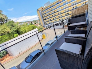 Ein Balkon mit Korbmöbeln, Blick auf einen Parkplatz und ein gelbes Gebäude im Hintergrund.