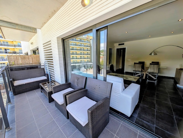 A balcony with wicker furniture, a glass door, and a view of a building.