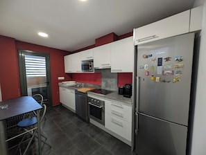 Eine kleine Küche mit weißen Schränken, einem Edelstahlkühlschrank, einer Mikrowelle und einer Kaffeemaschine.