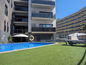 A modern building with multiple balconies, a swimming pool, and outdoor seating areas.