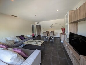 A modern living room with a sofa, coffee table, TV, and dining area.