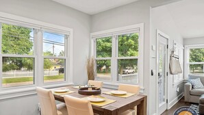 A dining area with a table set for four, large windows, and a view of a fenced yard. - Walk to Lake & Downtown · 3BR Home Sleeps 8 (Lake Geneva)