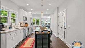 A modern kitchen with white cabinets, a central island, and a view to the dining area. - Walk to Lake & Downtown · 3BR Home Sleeps 8 (Lake Geneva)