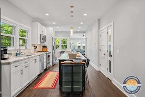 Une cuisine moderne avec des meubles blancs, un îlot central et une vue sur la salle à manger.