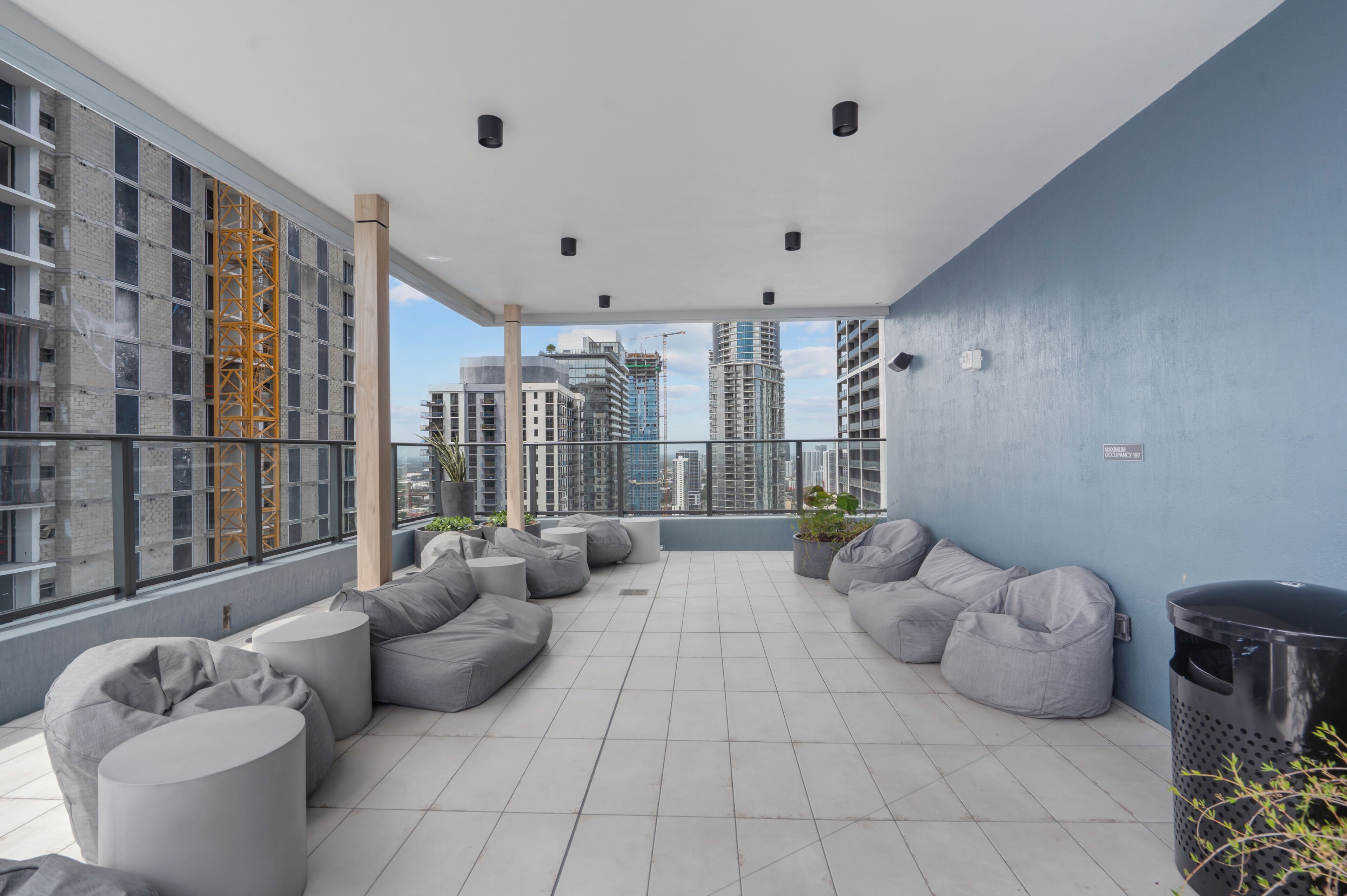 A rooftop terrace with grey bean bag seating, a trash bin, and a view of high-rise buildings.