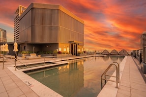 Un edificio moderno con piscina, zona de estar al aire libre y un cielo al atardecer.