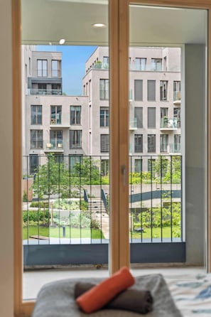 Ein Schlafzimmer mit Balkon, einem Bett mit Kissen und Blick auf einen modernen Gebäudekomplex.