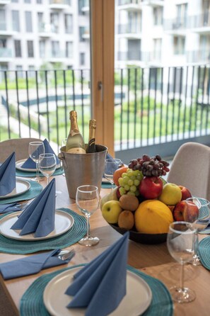 Ein Esstisch gedeckt mit blauen Servietten, Tellern und Gläsern, einer Obstschale und einem Champagnerkühlbag mit Flaschen.