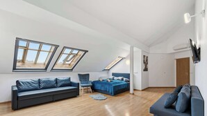 Un espai tipus loft amb sostre alt, lluminàries a la teulada, un sofà, un llit i una cadira.