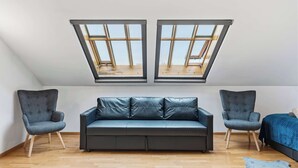 Habitació amb un llit amb altell, un sofà, dues butaques i lluminàries al sostre.