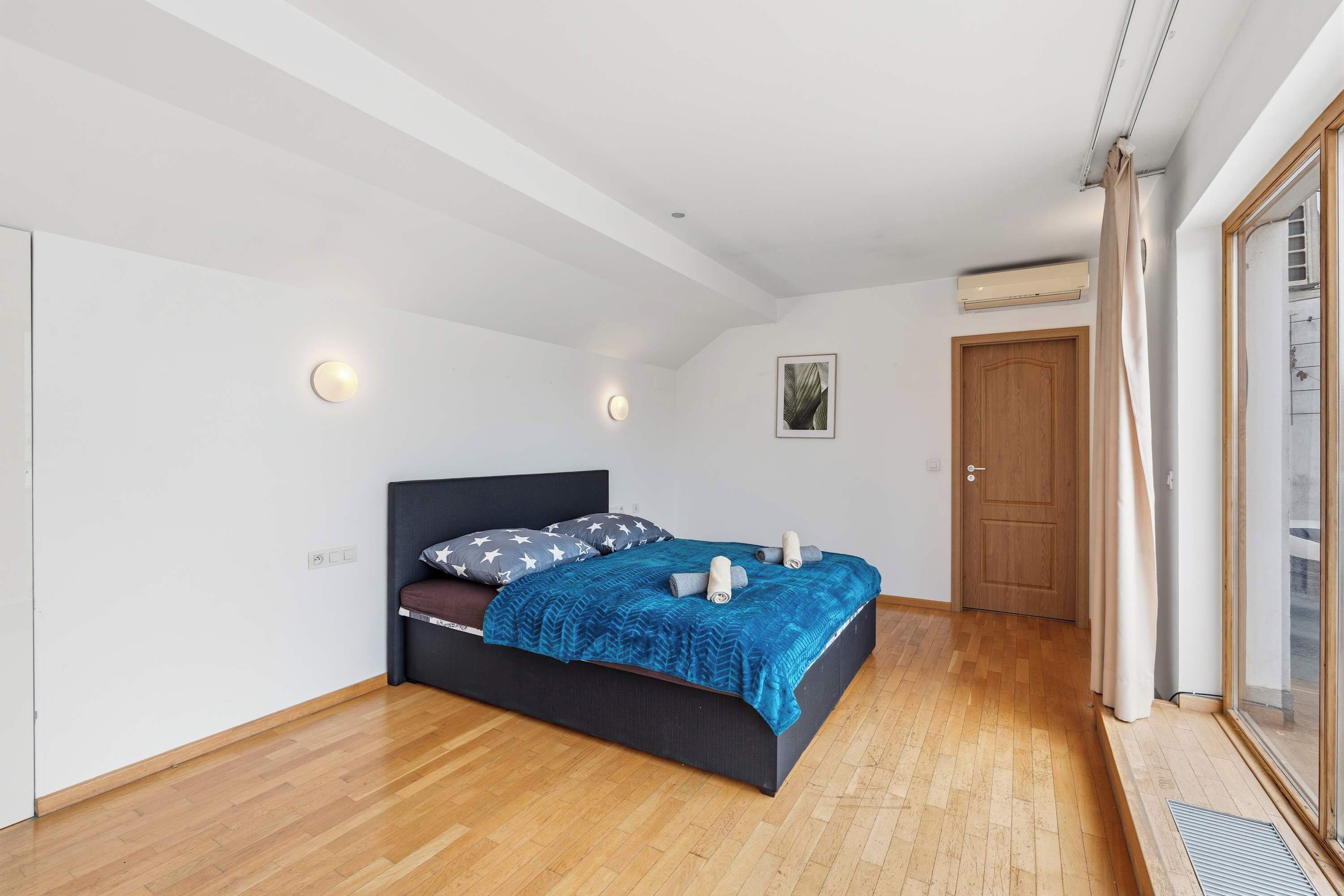 Un dormitorio con una cama, una puerta de madera y una ventana con cortinas.
