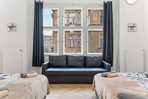Ein Zimmer mit großem Fenster, einer Couch, zwei Betten und Blick auf Gebäude.