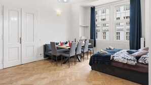 Um quarto com mesa de jantar, cadeiras, uma cama, janela com cortinas e luminária suspensa.
