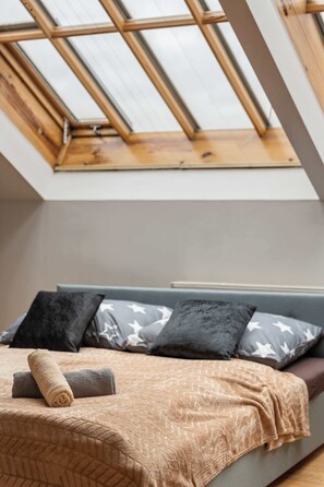 Une chambre avec une lucarne, un lit recouvert d’une couvre-lit à motifs et des oreillers décorés d’étoiles.