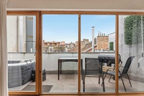 Un balcon avec un jacuzzi, une table et des chaises, offrant une vue sur le paysage urbain.