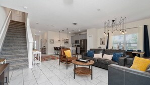 A modern living room with a staircase, a dining area, and a kitchen. - 5BR ChampionsGate Home with Pool & Water Park (Championsgate)
