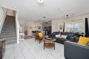 A modern living room with a staircase, a dining area, and a kitchen. - 5BR ChampionsGate Home with Pool & Water Park (Championsgate)