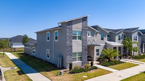 A modern two-story residential building with a stone facade, multiple windows, and a well-maintained lawn. - 5BR ChampionsGate Home with Pool & Water Park (Championsgate)