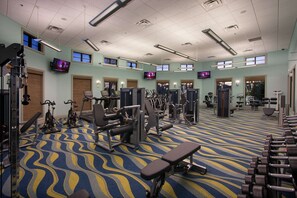 A gym with various exercise equipment, a patterned carpet, and multiple TV screens on the walls. - 5BR ChampionsGate Home with Pool & Water Park (Championsgate)