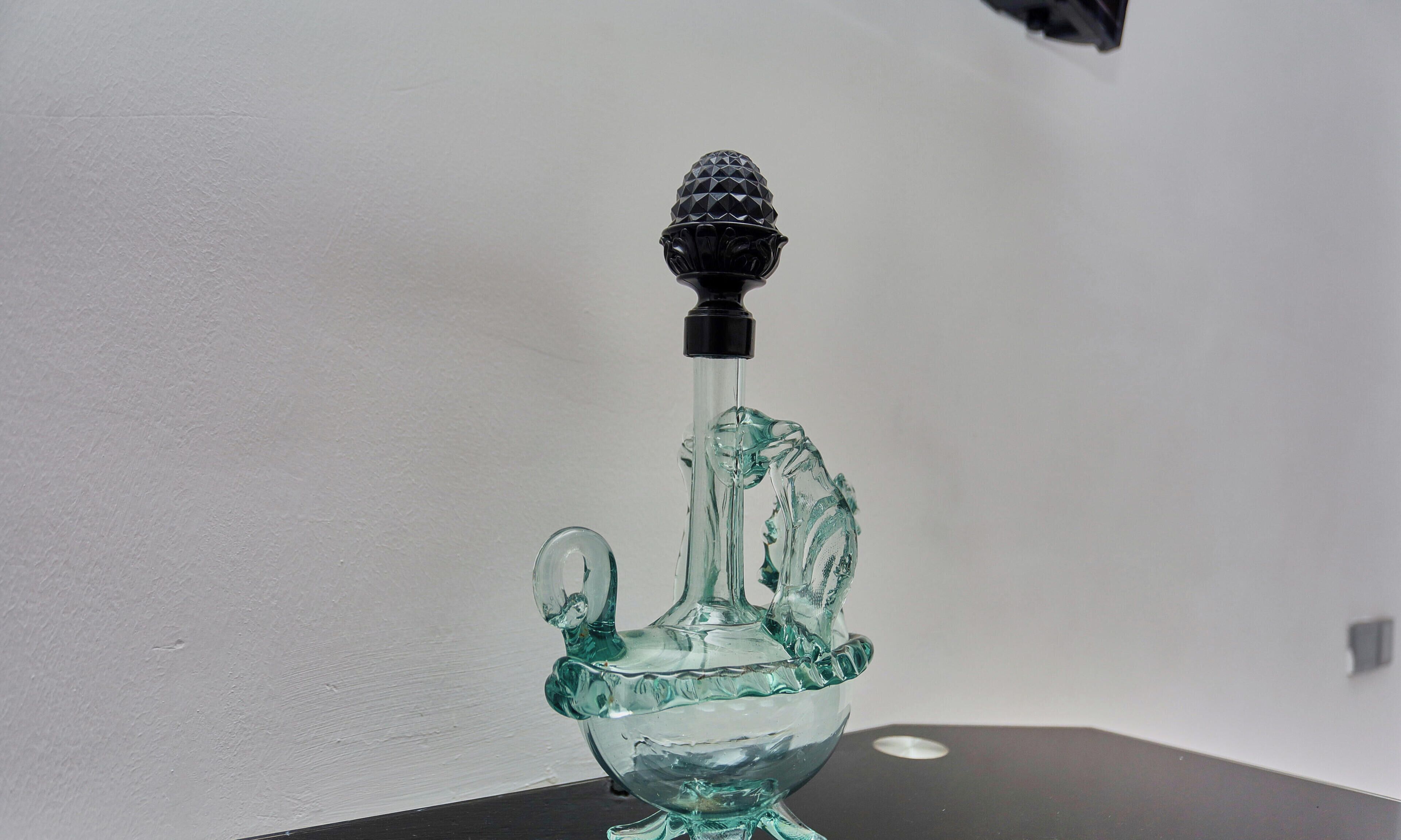 A clear glass object with a black top, possibly a decorative item, on a flat surface against a plain background.