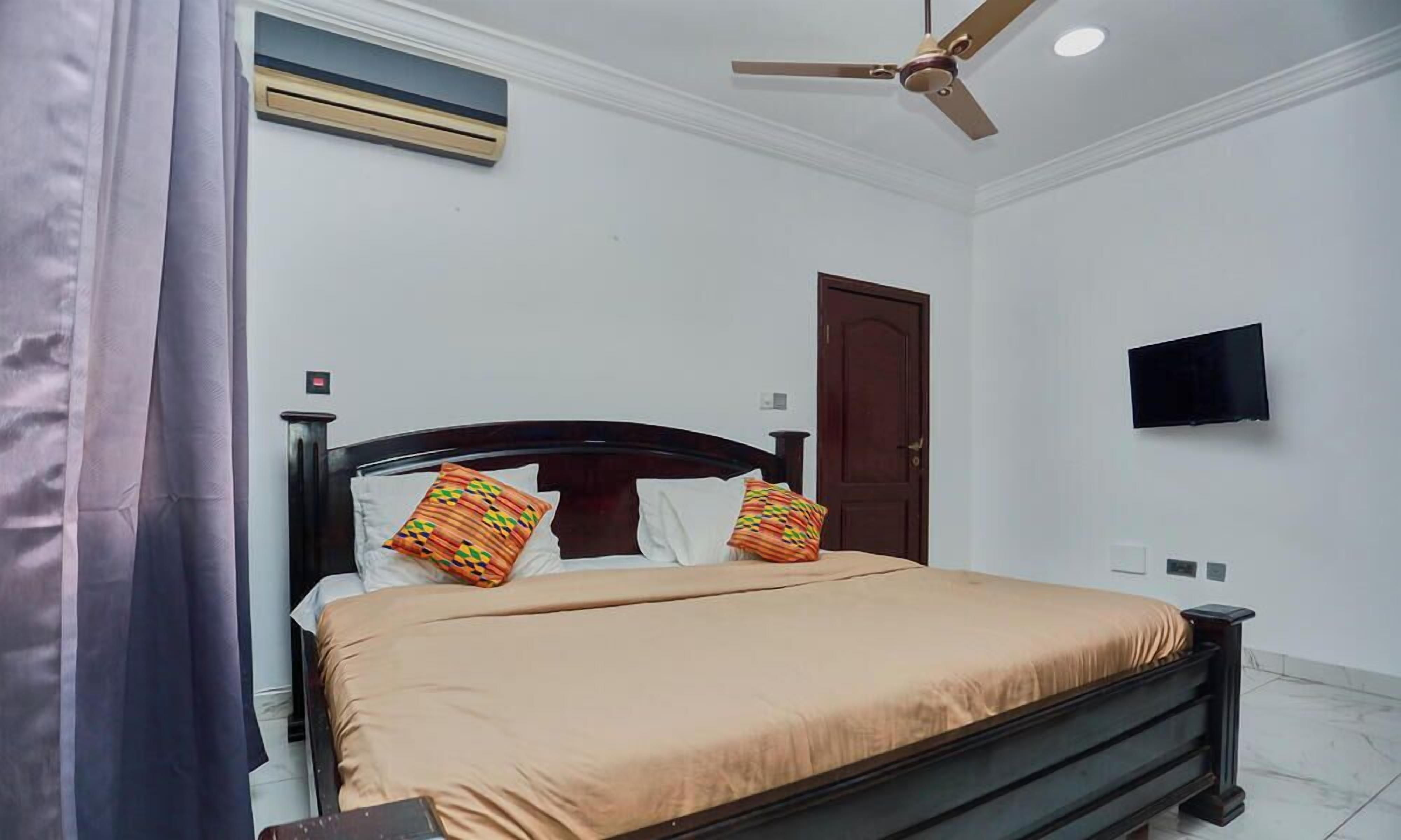 Un dormitorio con cama, ventilador de techo, televisor y puerta.