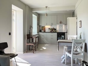 Eine moderne Küche mit weißen Schränken, einem Essbereich mit Tisch und Stühlen sowie einer kleinen Sitzecke mit Sessel und Sofa.