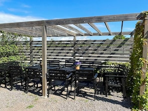 A covered outdoor seating area with wooden benches and tables, surrounded by a wooden pergola structure. - 5 Star Holiday Home in Morbylanga (Morbylanga)