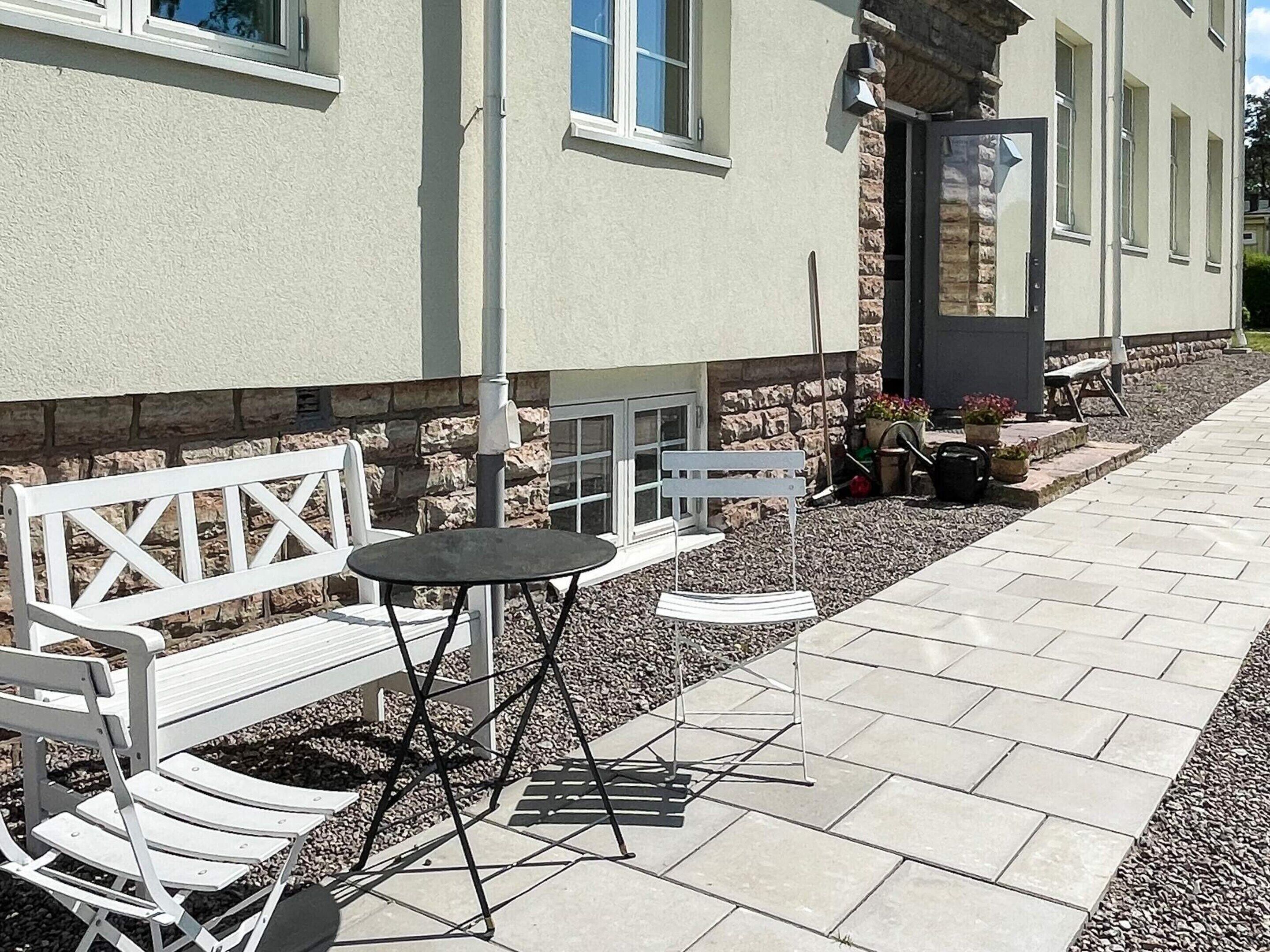 An outdoor seating area with a white bench and a small round table, a stone wall, and a paved walkway.