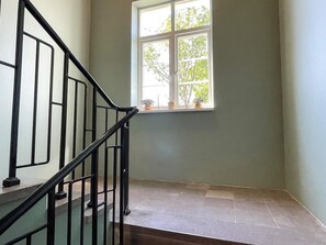 Eine Treppe mit schwarzen Geländern, ein Fenster mit Blick auf Bäume und eine schlichte Wand.
